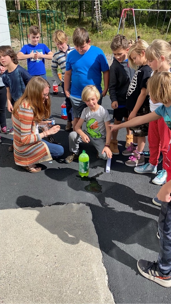 students and  teacher gathered around soda bottle 